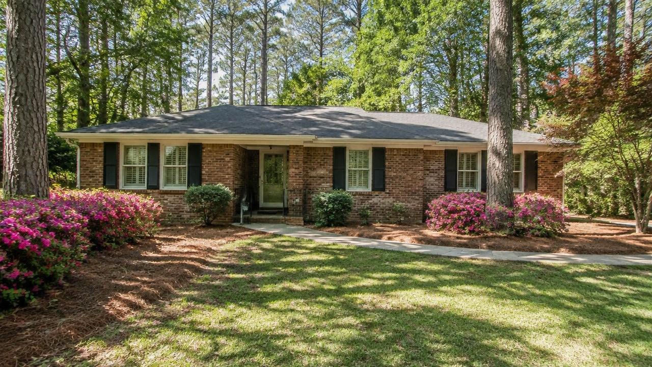 A mature brick ranch home with azaleas and tall pines