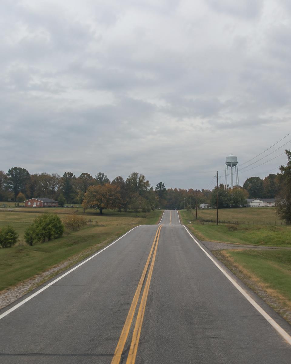 A two-lane road through open fields under a cloudy sky