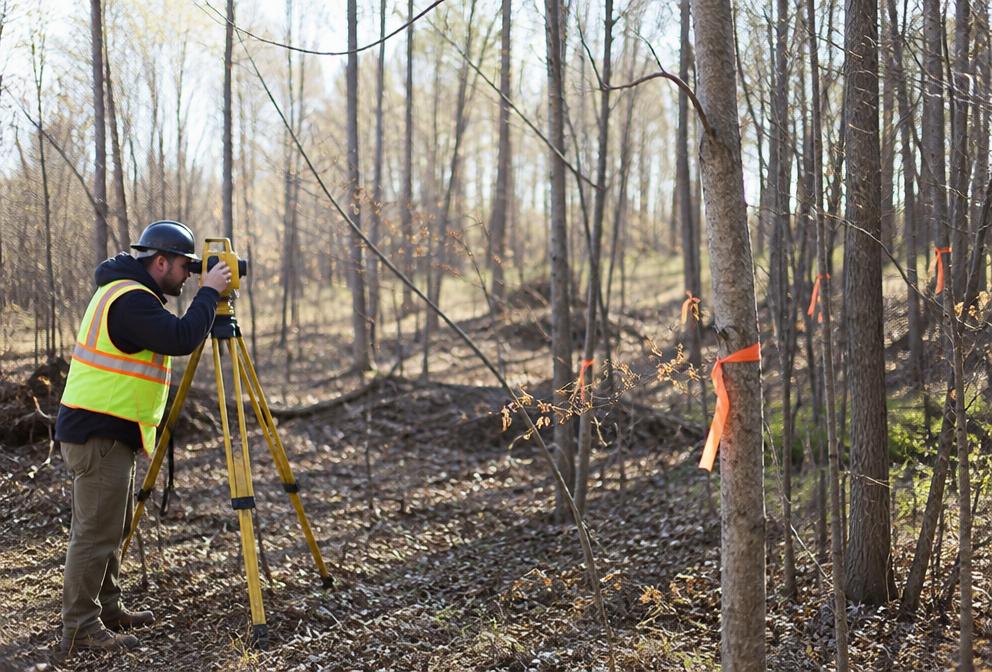 A surveyor working on a wooded vacant lot